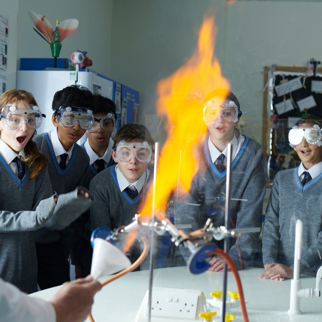 Belmont, Mill Hill Prep pupils in a science lab classroom wearing safety goggles, watching with excitement as a controlled flame experiment takes place, demonstrating hands-on learning in science.