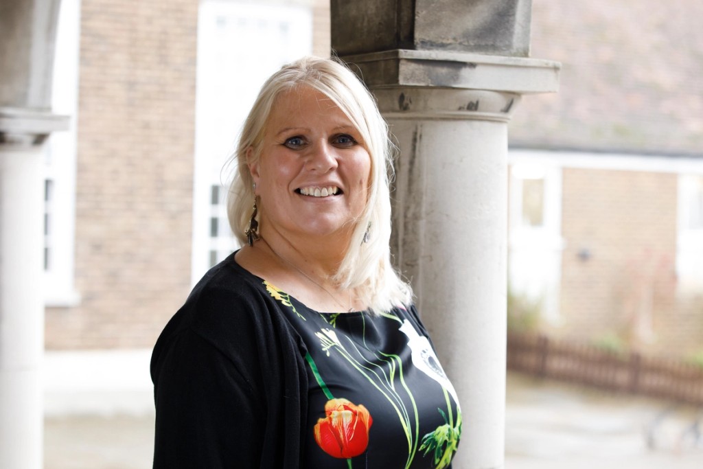 Portrait of Mrs. Libby Russo, Assistant Head (Pupil and Staff Wellbeing) and Deputy Designated Safeguarding Lead at Mill Hill School, smiling under a columned walkway, wearing a floral-patterned top and black cardigan.