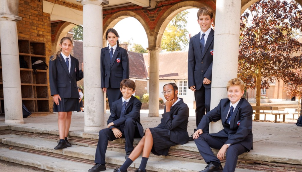 Group of six students in formal uniforms sitting on the steps outside, smiling and posing for a group photo at Belmont, Mill Hill Prep.