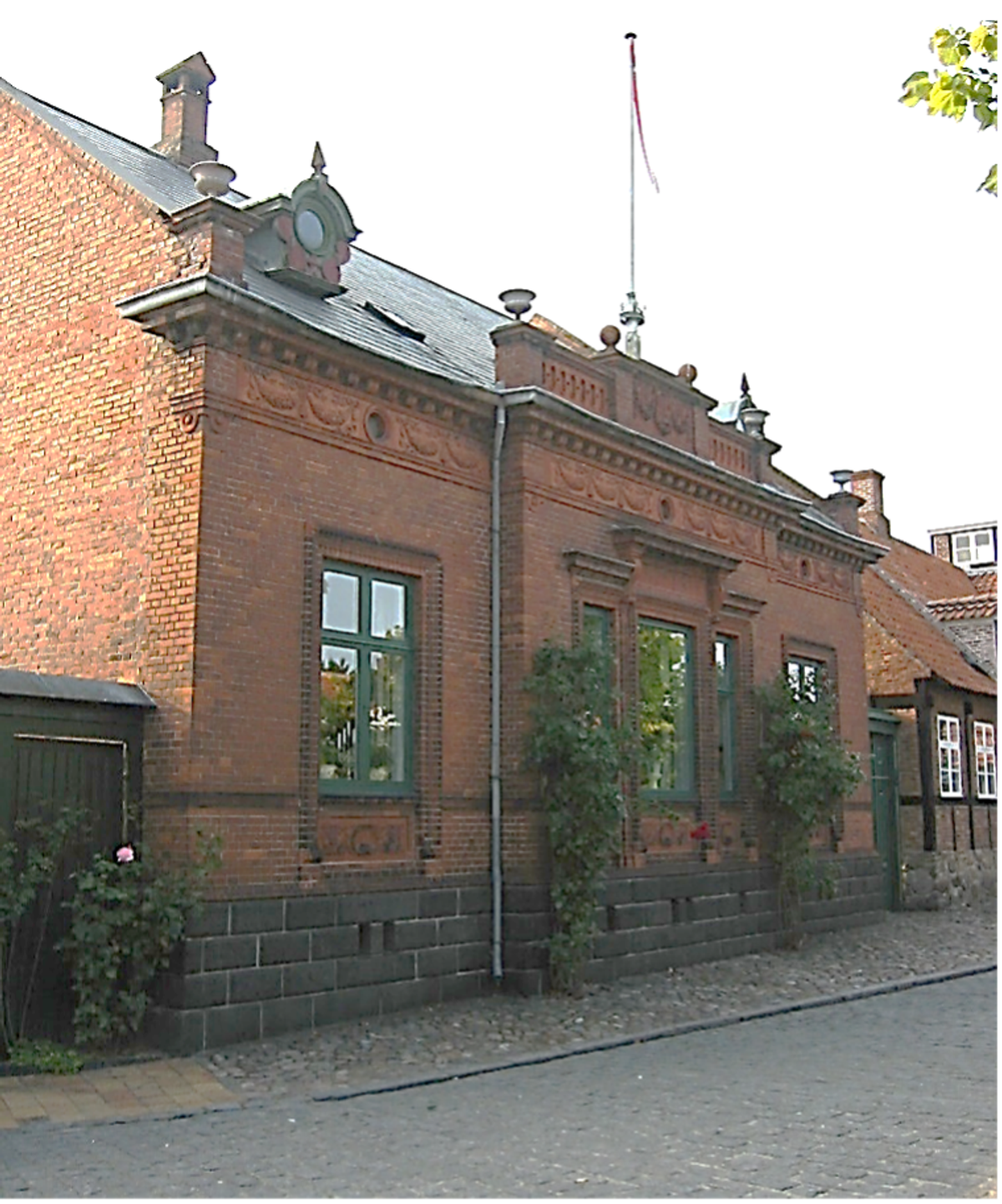 Ill. 3. Hus i Rønne med alle historicismens mest prestigefulde materialer og elementer. Hovedfacade med terracotta-detaljer, gesims, vinduesindfatninger, facadebånd. Midterrisalit med attika og zinkvaser og murede pinakler med zinkvaser i gavlene. Skifertag og kviste med zinkdetaljer, muret og dekoreret skorstenspibe, dekoreret granitsokkel og underfacade. Huset er et kulturhistorisk eksempel på historicismens pyntesyge, men også klassiske viden om og opbygning af facader og detaljer. Foto: Søren Vadstrup
