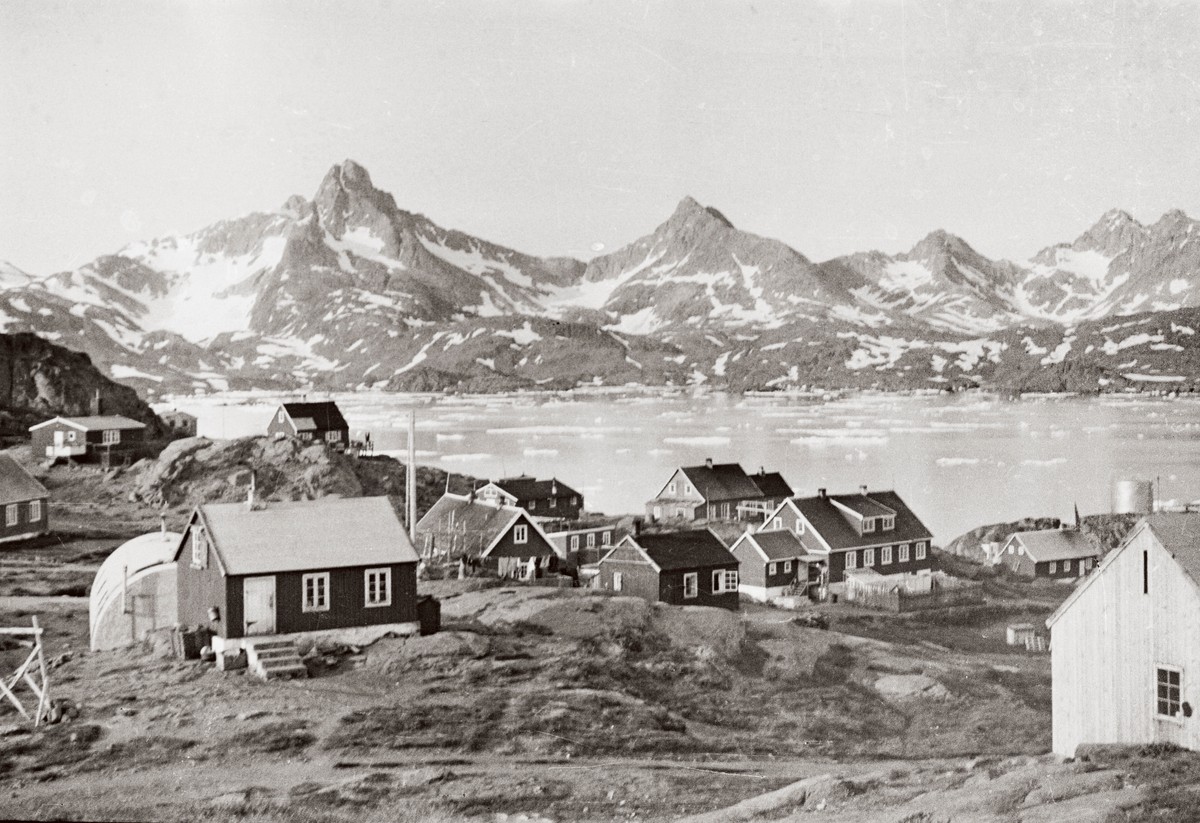Ill. 12. Den centrale del af ”kolonien”, altså byen Tasiilaq, ca. 1954. Her er mange interessante bygninger: Kirken til højre i billedet, kolonibestyrerens bolig (med kvisten), og forskellige boliger til de danske udsendte. På billedet ses også flere selvbyggerhuse og den amerikanske Quonset hut.