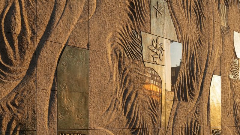Close detail of a textured limestone and bronze facade on a Manhattan residential street, warm late afternoon light, abs