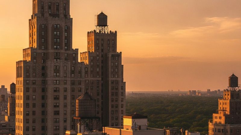 Editorial photograph of a slender Manhattan residential skyline at golden hour seen from a high terrace, setback masonry