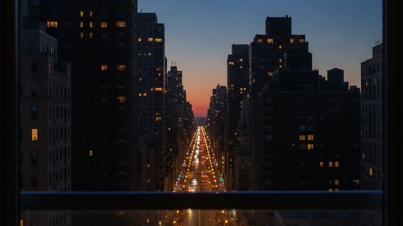 Editorial photograph of Park Avenue at dusk from a high residential window, the avenue's lights stretching north, apartm