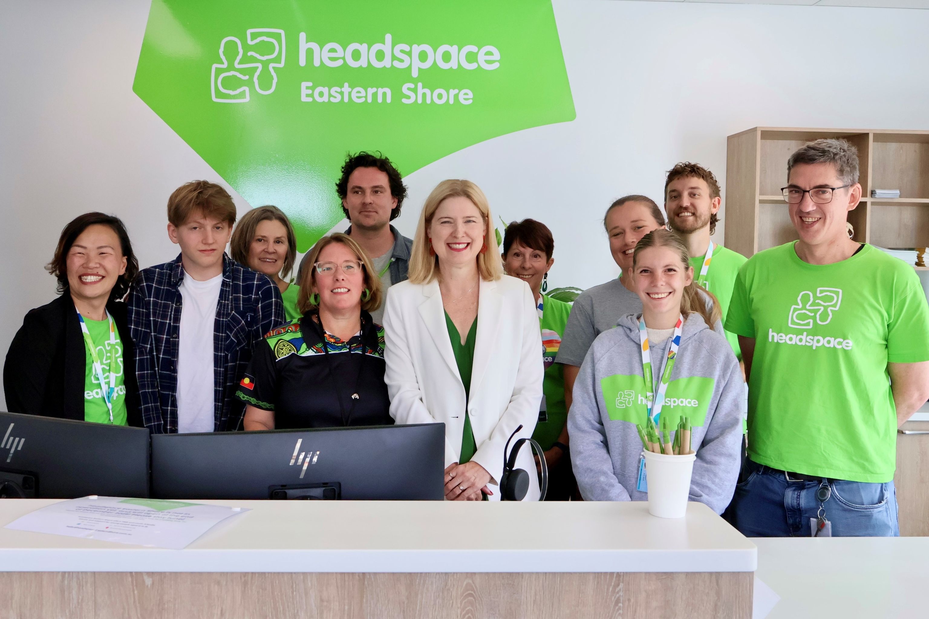 11 people are gathered behind a desk, in front of a large green "headspace Eastern Shore" sign. Most are wearing green headspace tshirts.