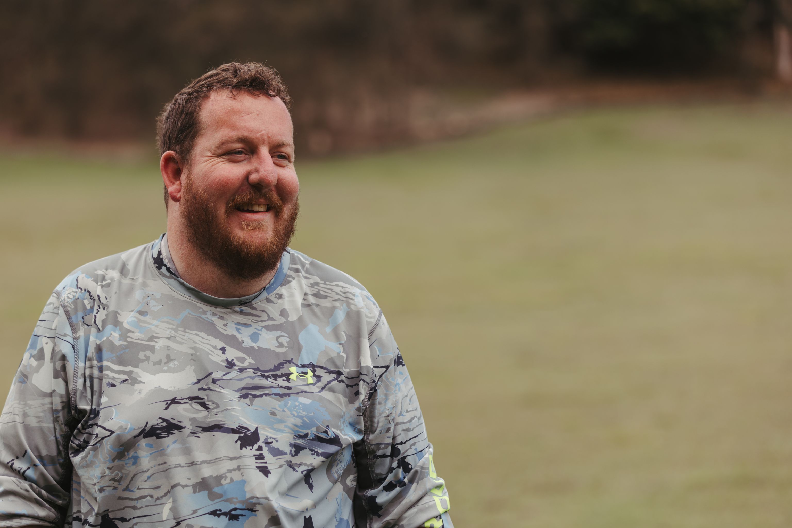 A man standing in a park smiling and looking slightly away from camera.