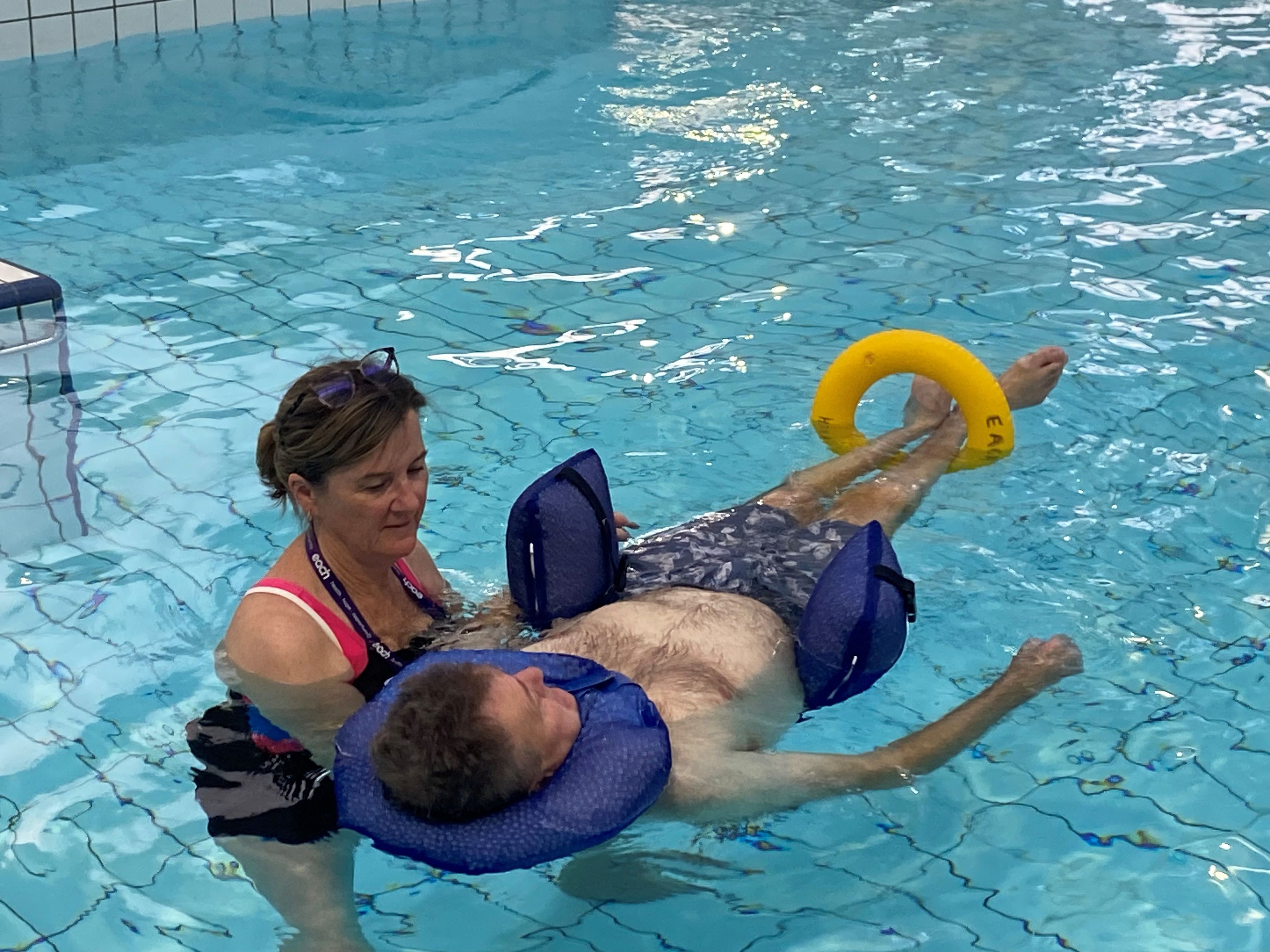 Physiotherapist Gabrielle is in a pool providing support to a man who is floating with his neck and legs supported.