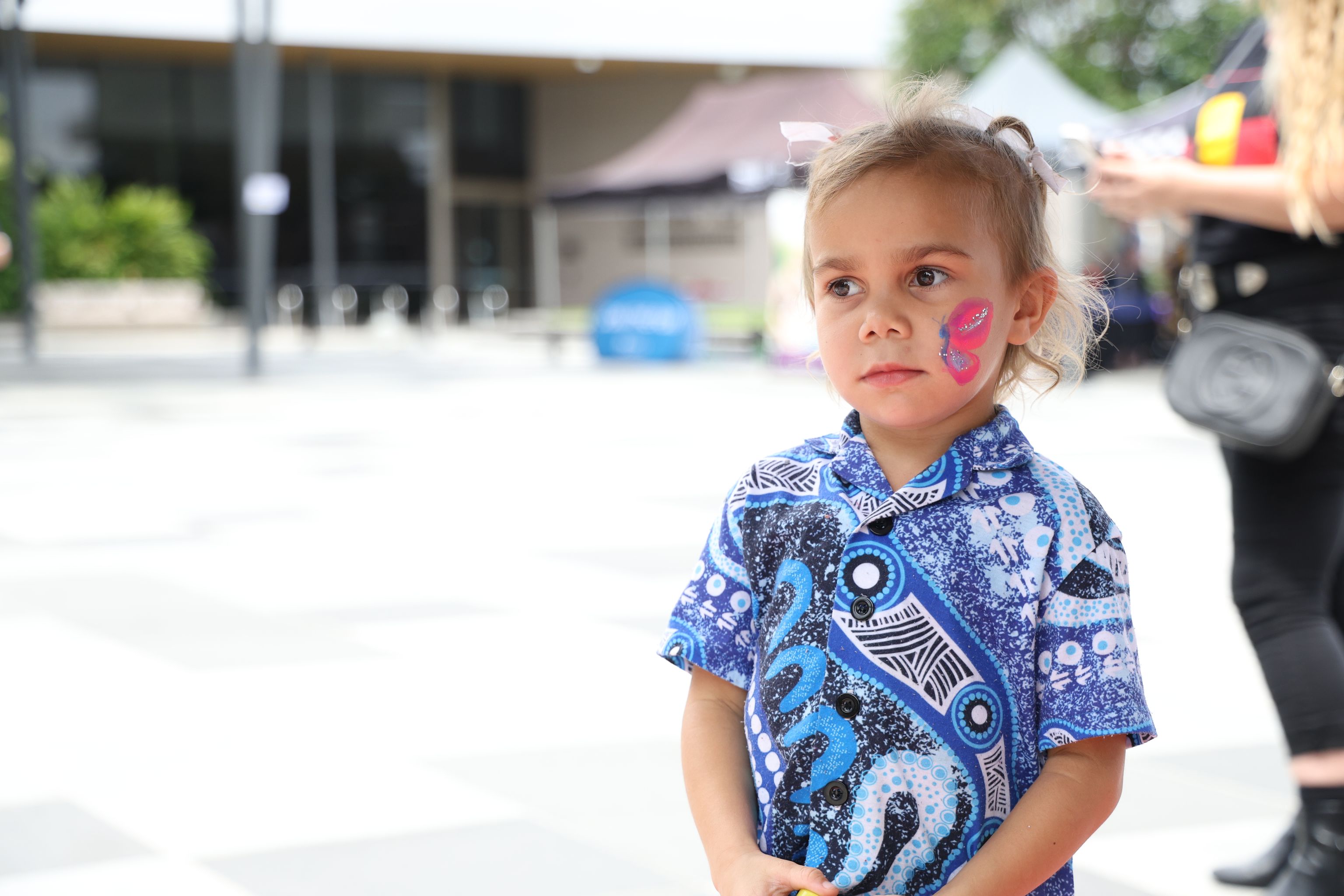 Young girl from the First Nations community with her face painted standing outside a centre looking away from camera