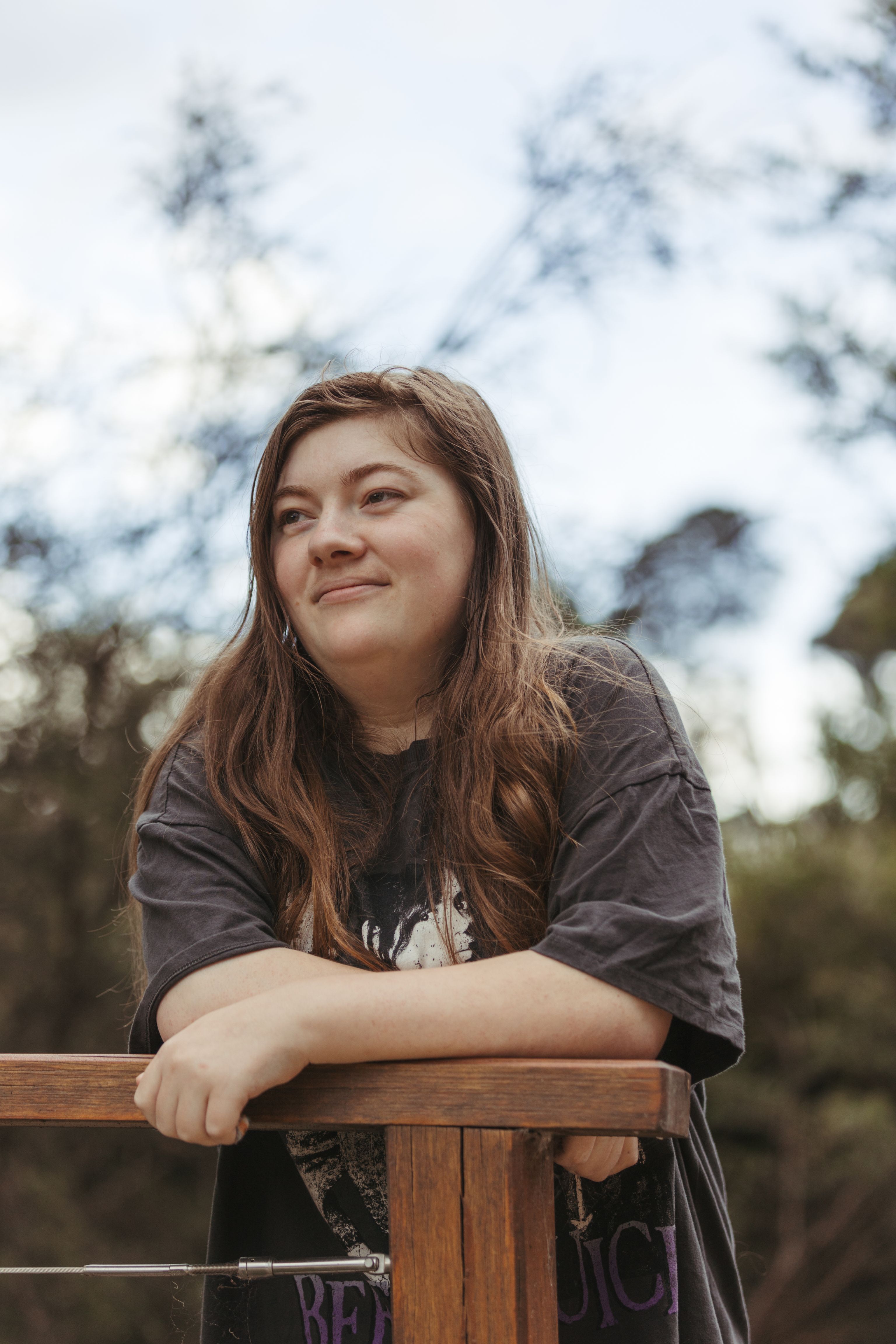 A young individual standing outdoors resting on a park railing, smiling and looking into the distance