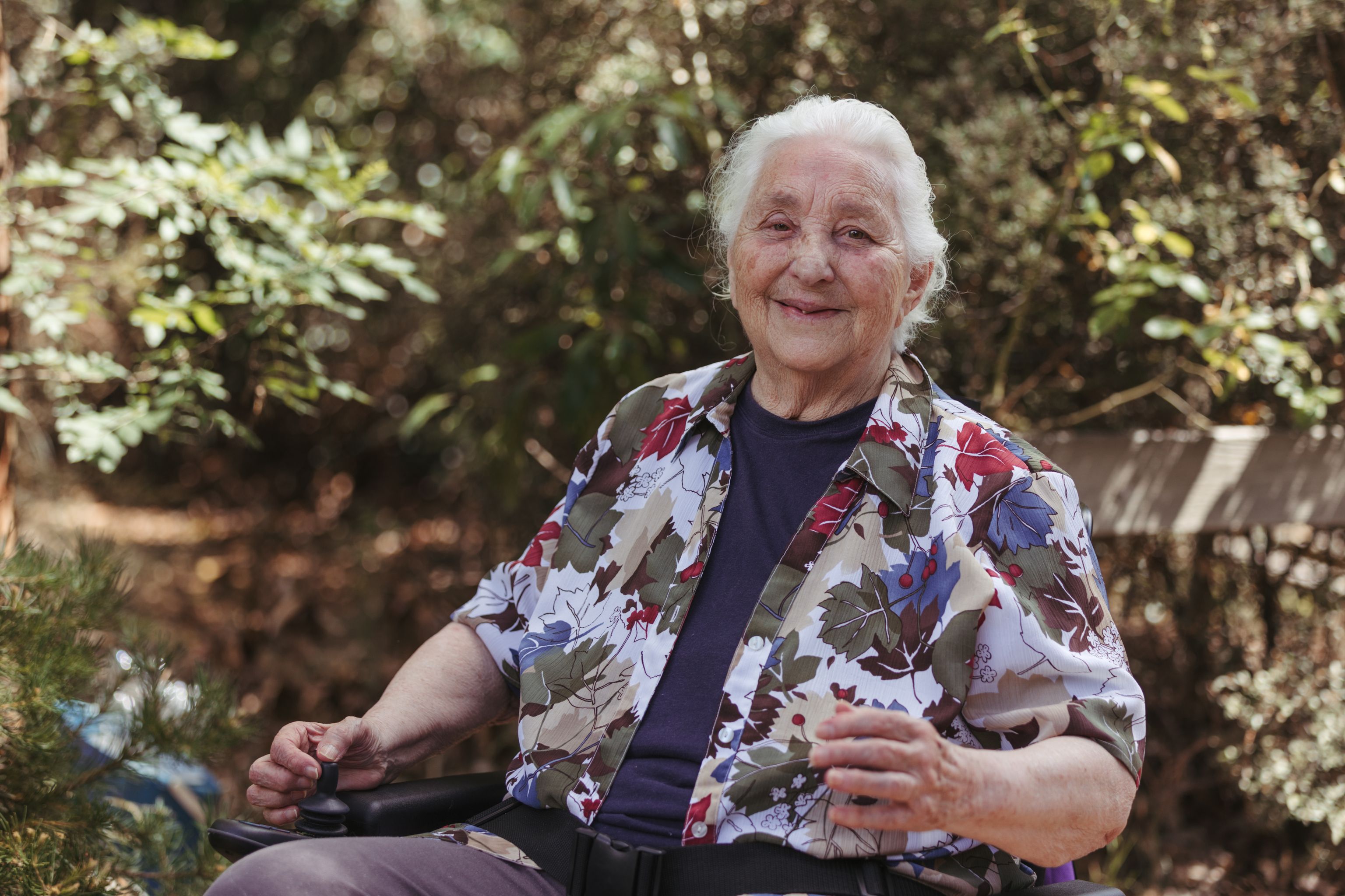Elida sits in her electric wheelchair outside. She has one hand on the controls, and a big smile on her face