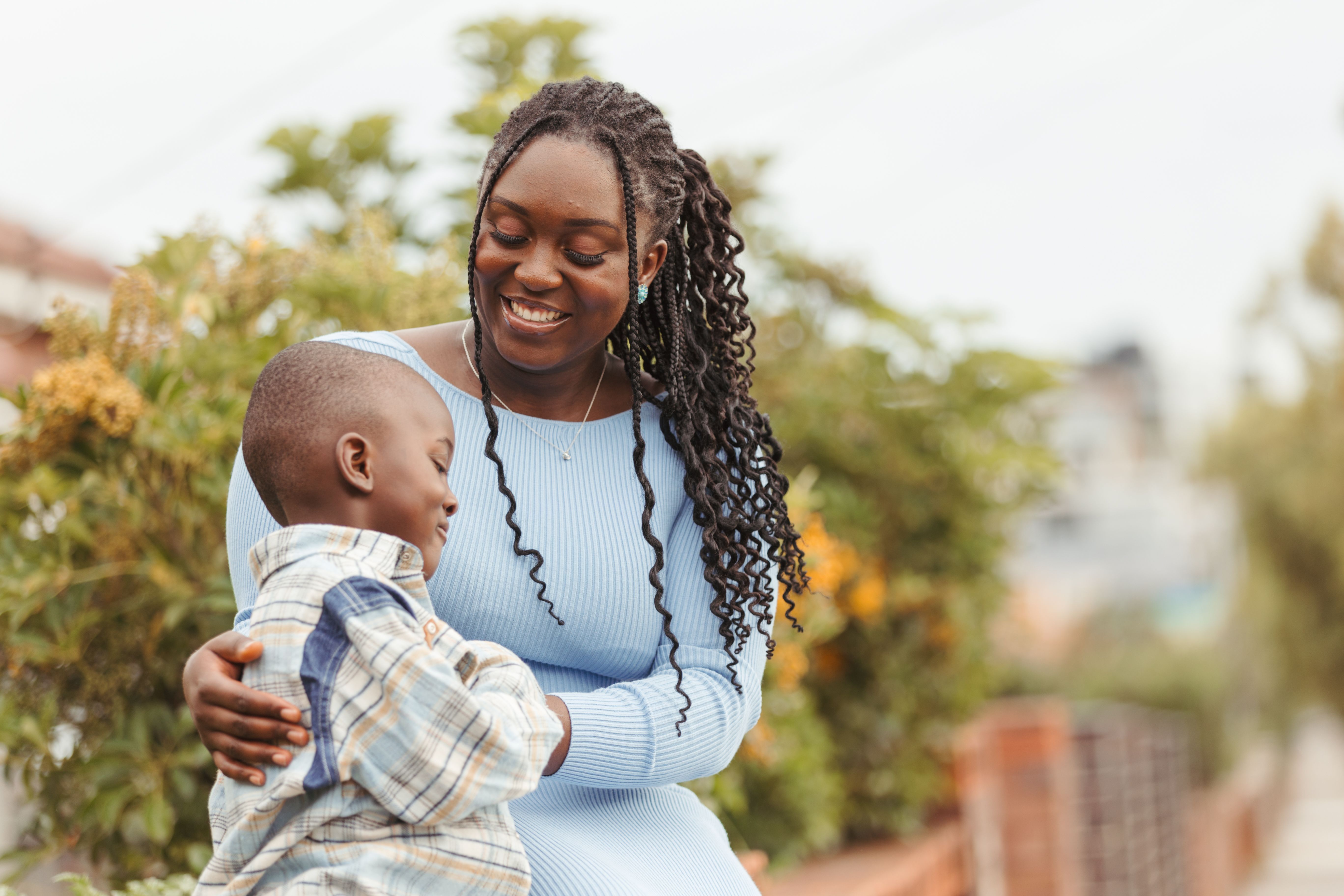 Young mother sitting with her young son on the fence outside their house