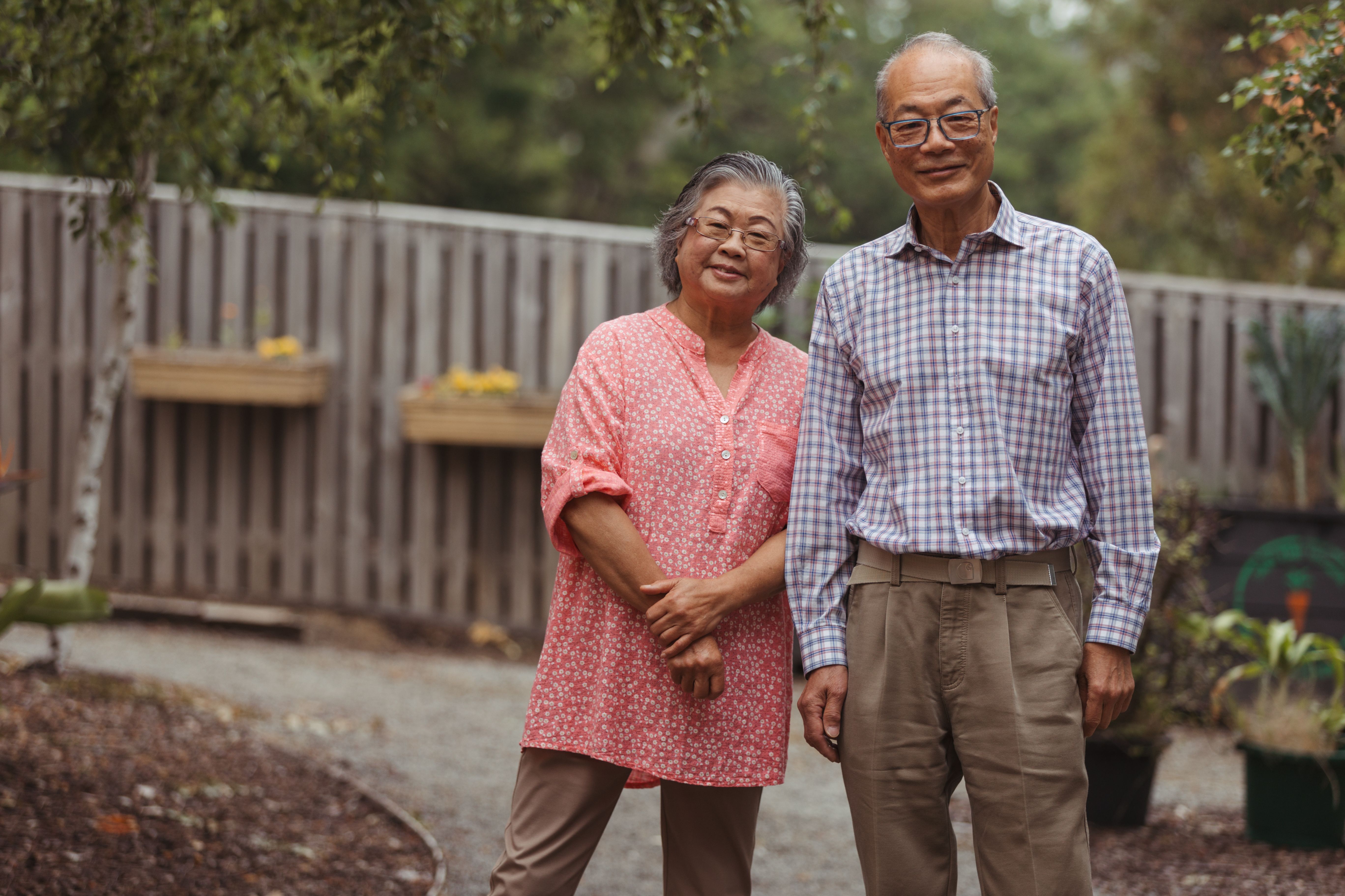 Older asian couple standing in a garden smiling