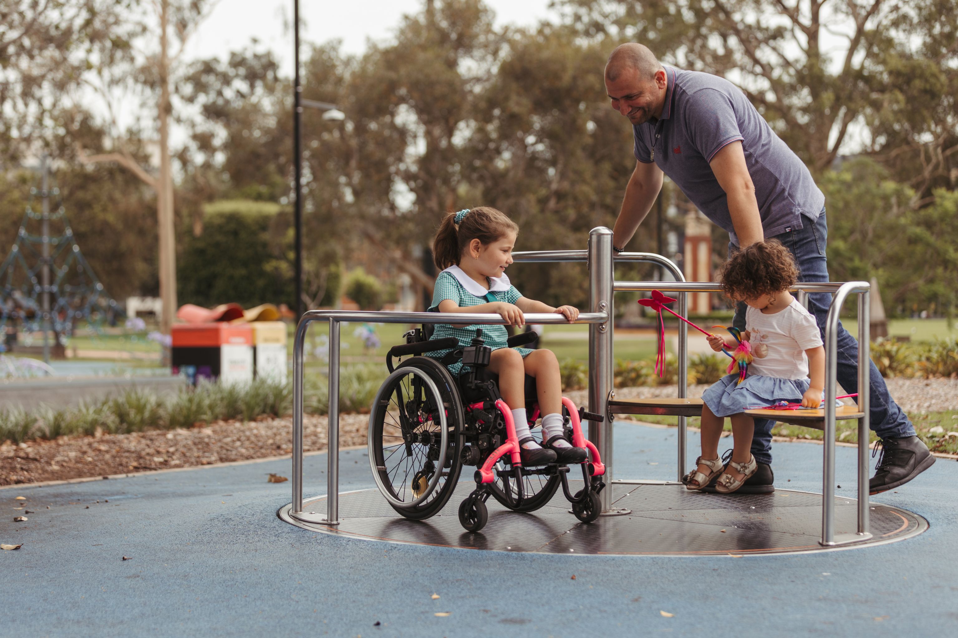 Father playing in a park with two young daughters with one in a wheelchair