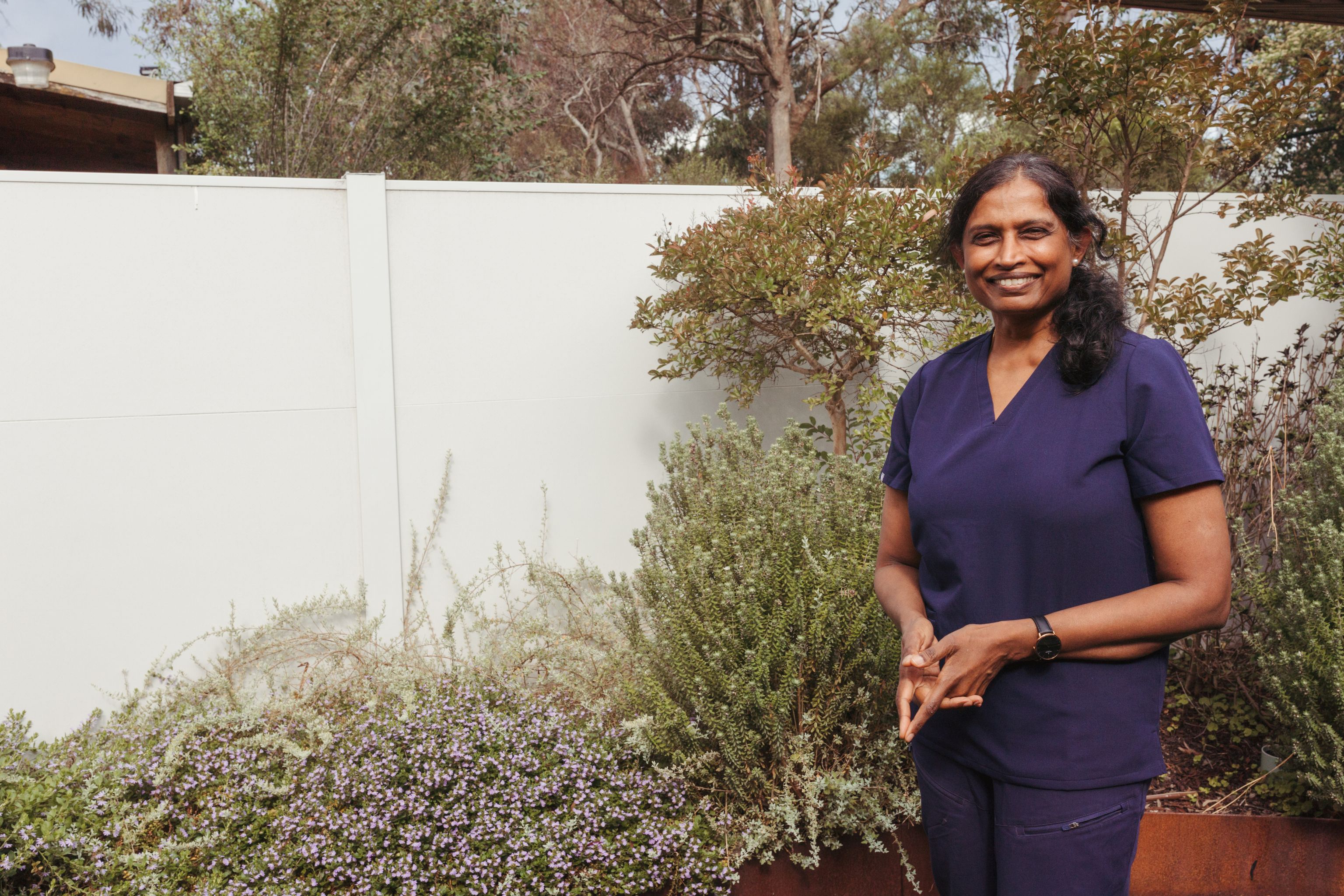An Each staff worker wearing scrubs standing outside and smiling into the distance
