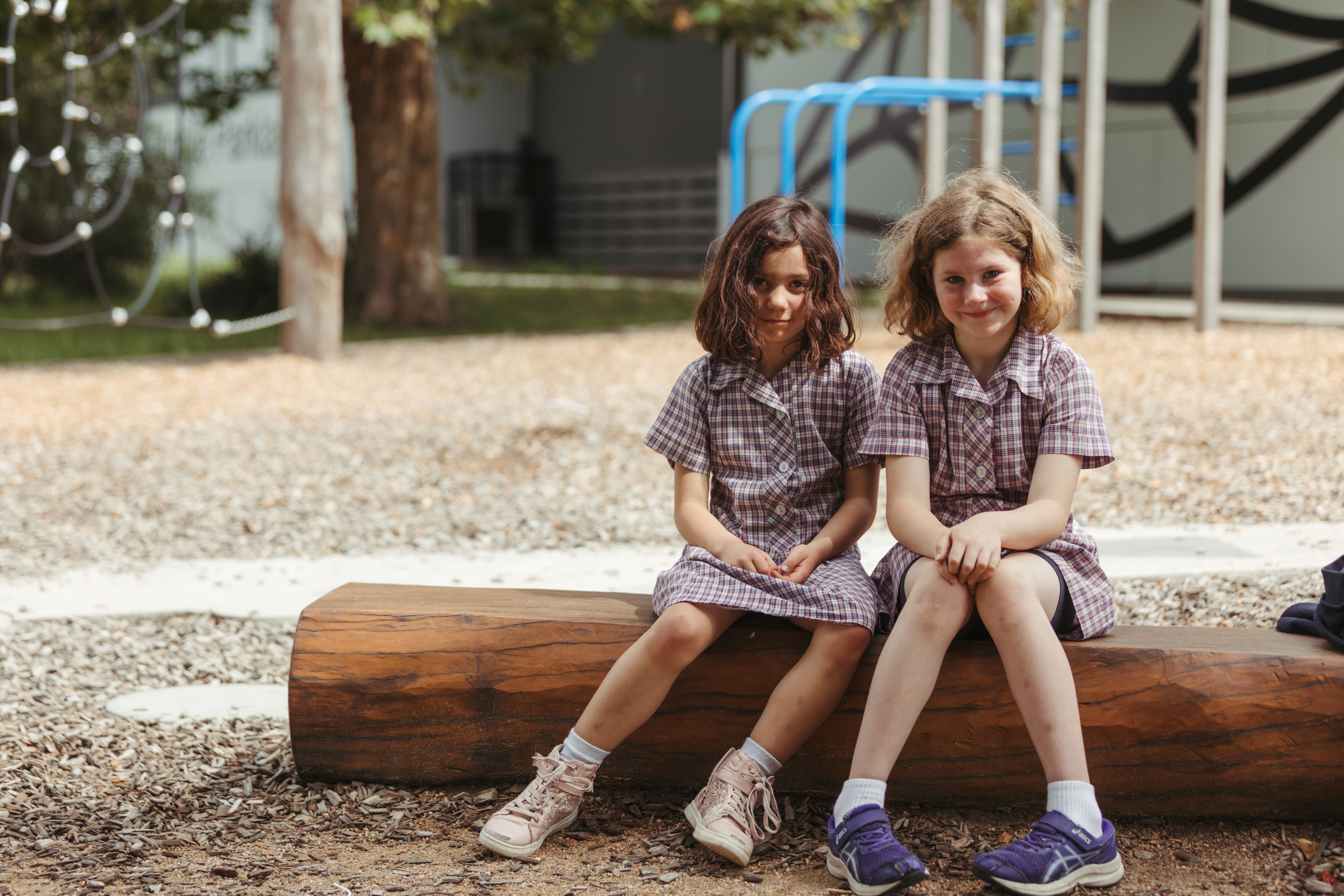 Two primary school girls sitting on a log in the school yard in their school uniforms