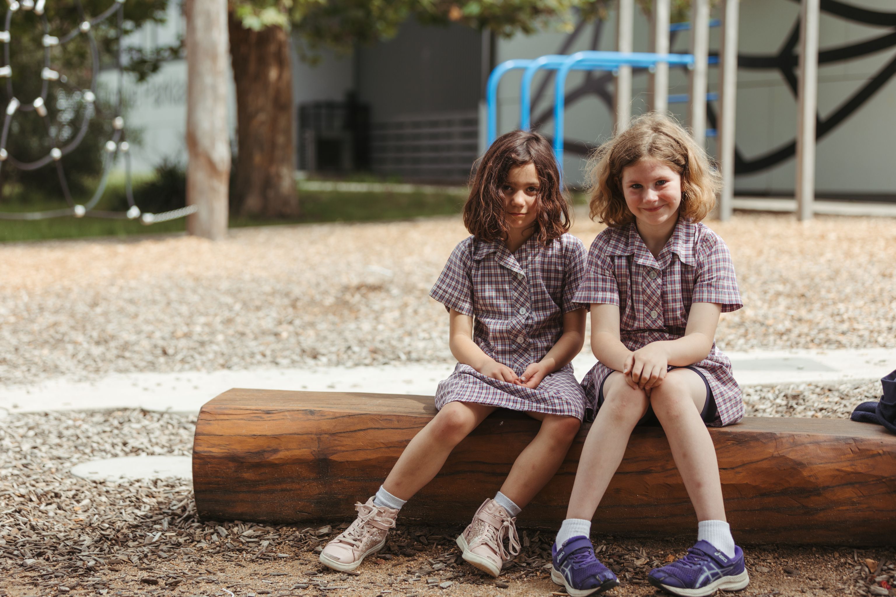 Two primary school girls sitting on a log in the school yard in their school uniforms