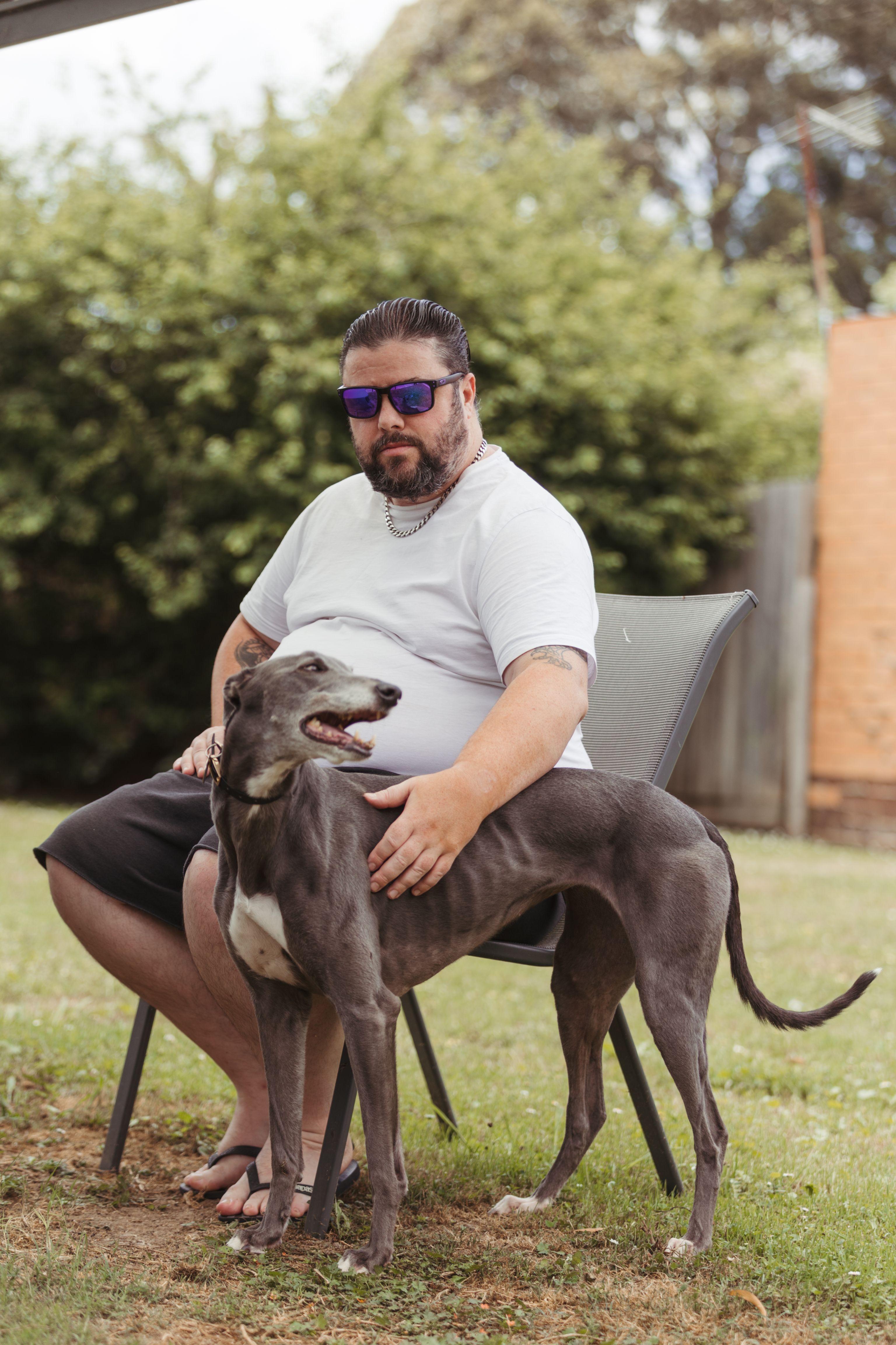 A blind man sitting on a chair outside padding a dog
