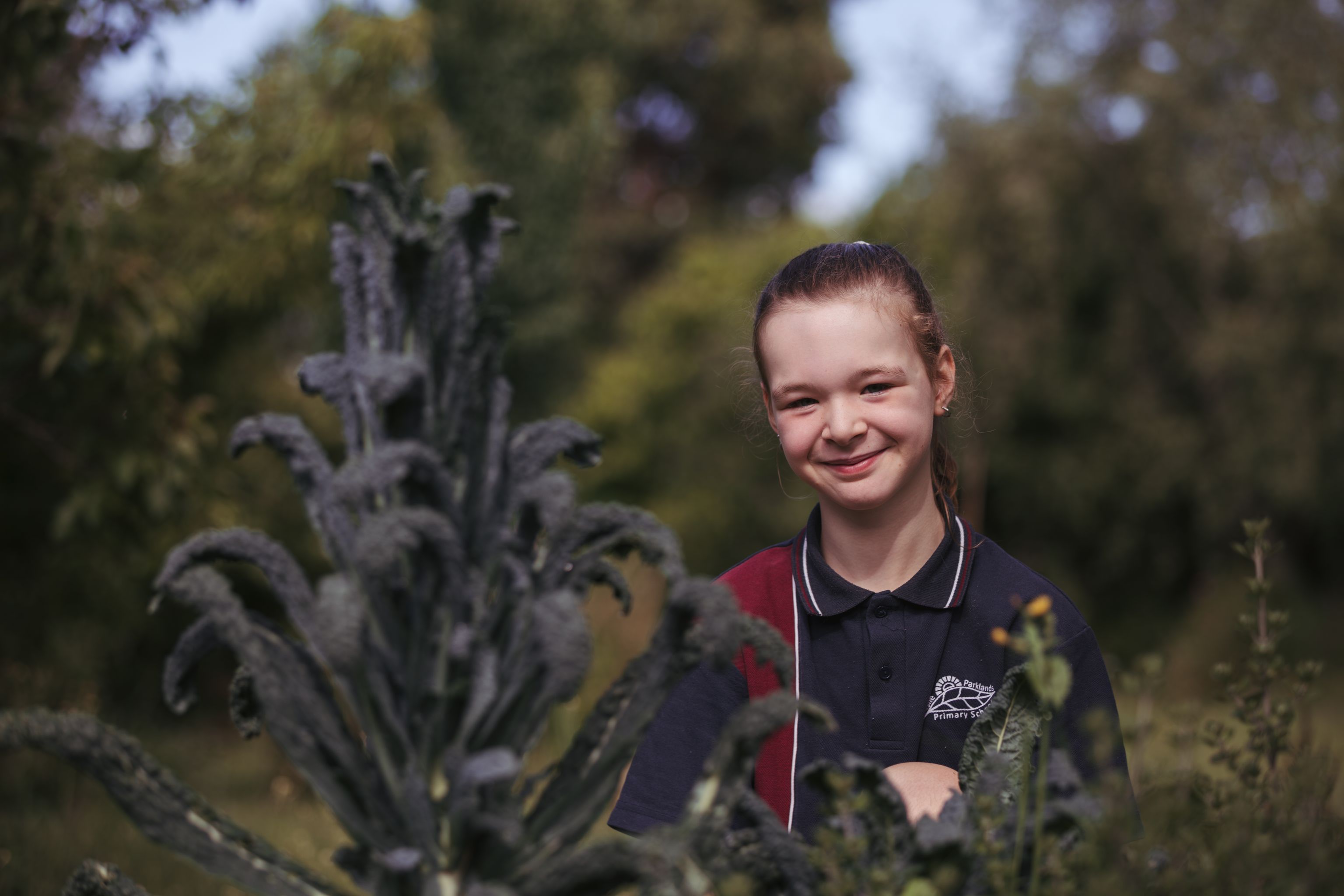 Smiling primary school girl, wearing a school uniform, standing in an edible garden.