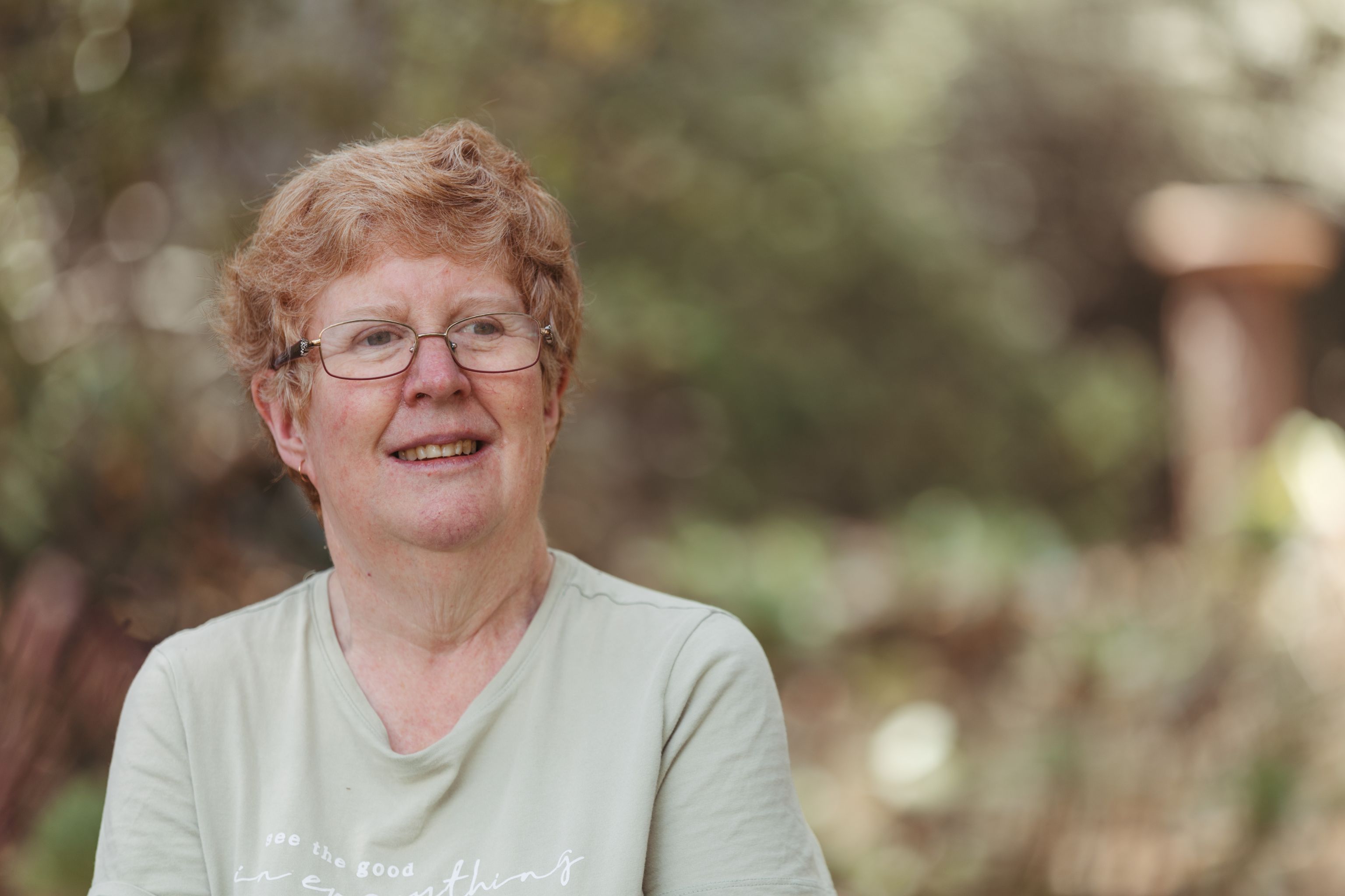 In her garden, Christine is smiling and looking ahead into the distance, like she's thinking about the future