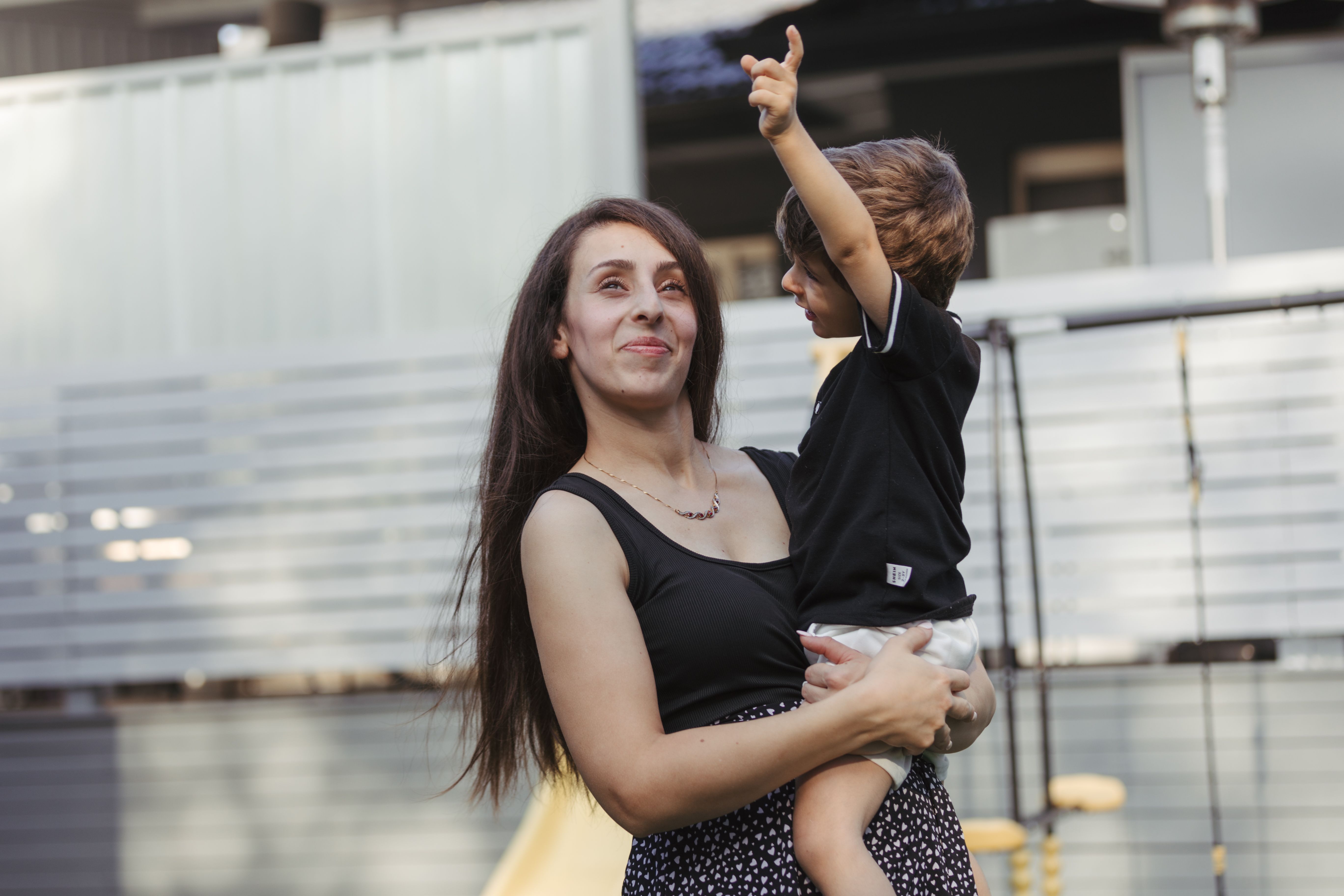 Young mother standing outside holding her son in her ams, the son has his hand up and they're both smiling
