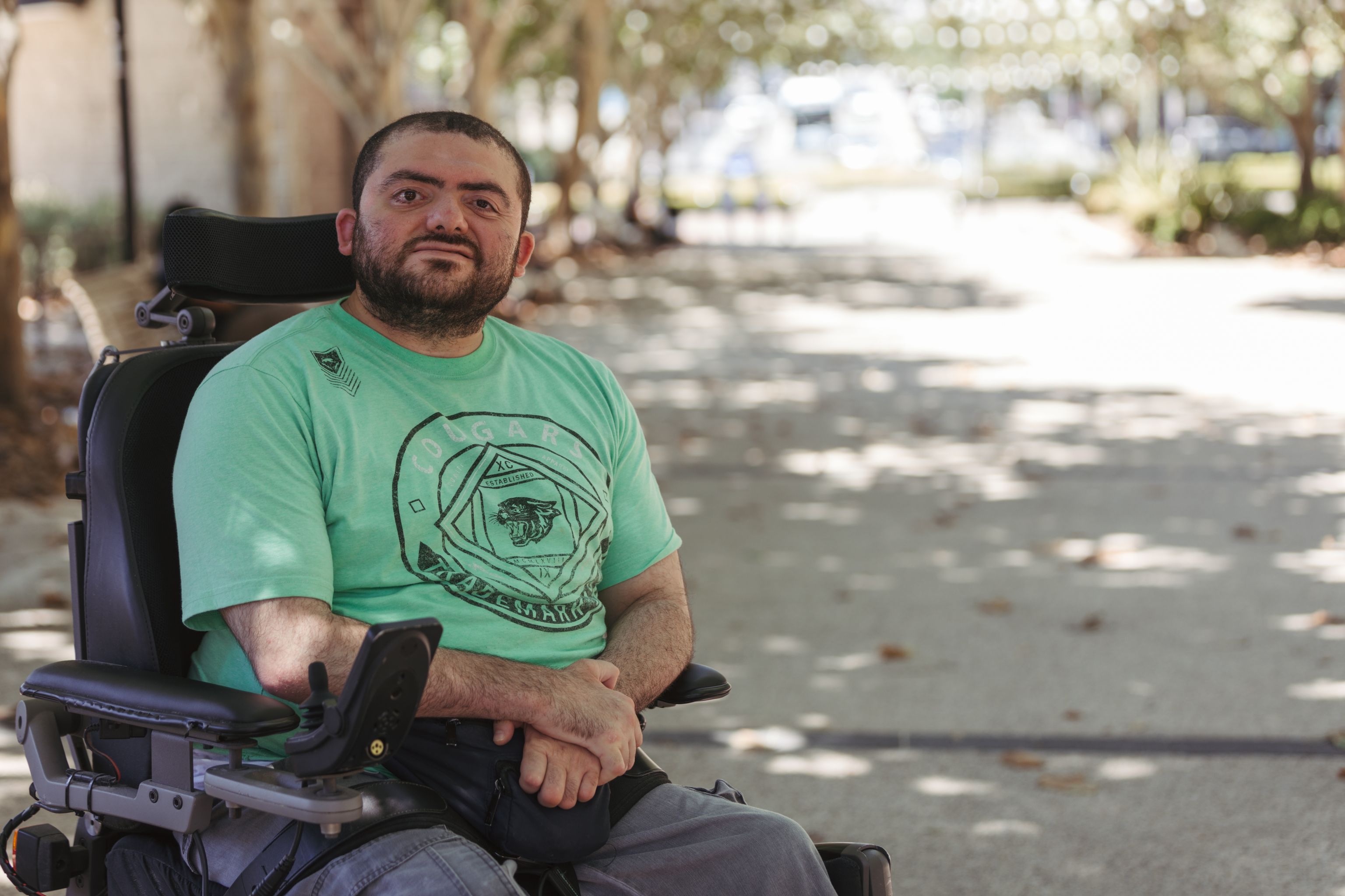 Young man with a disability sitting in a wheelchair outdoors smiling at the camera