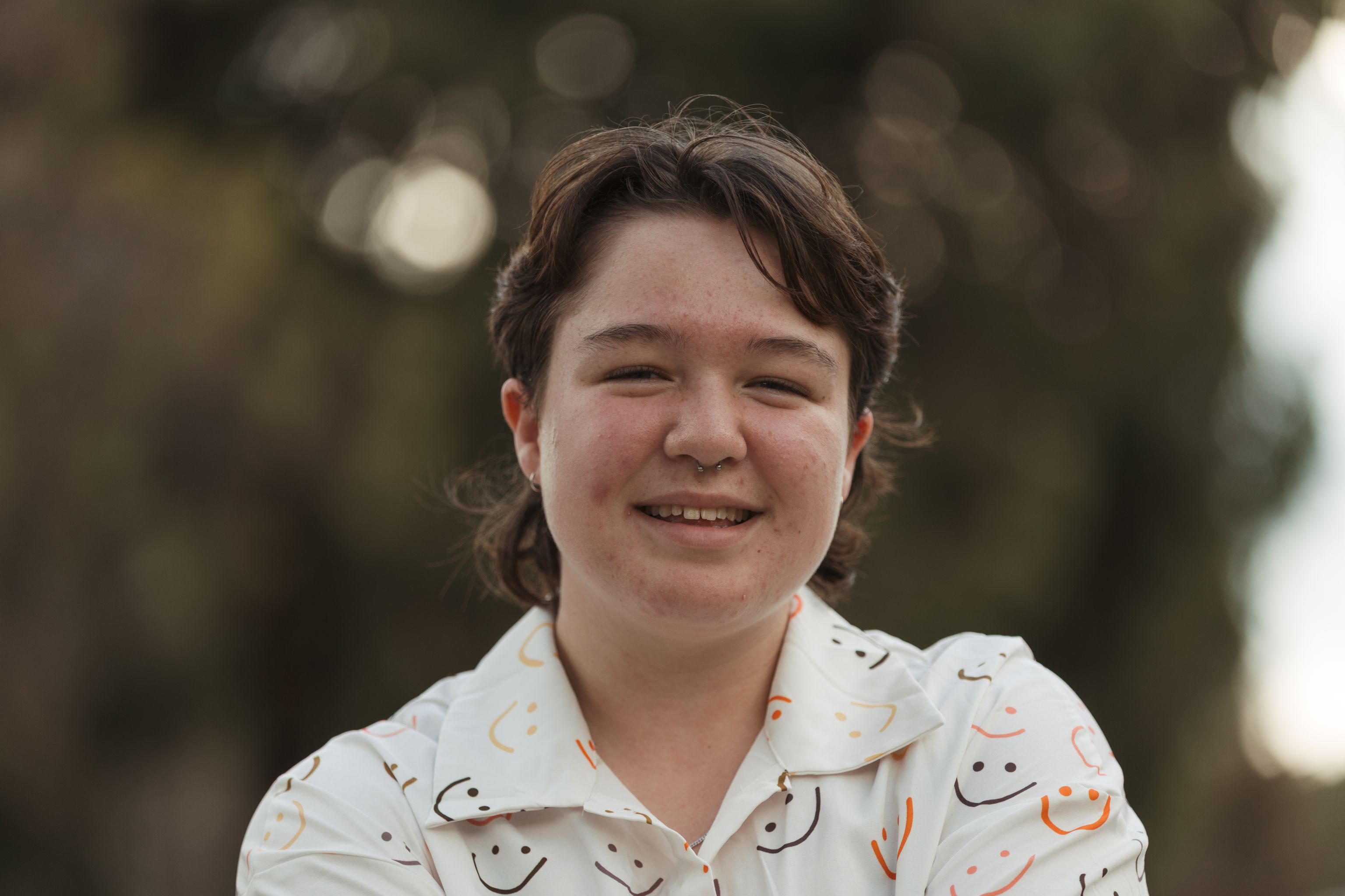 A young individual, standing outside smiling at the camera