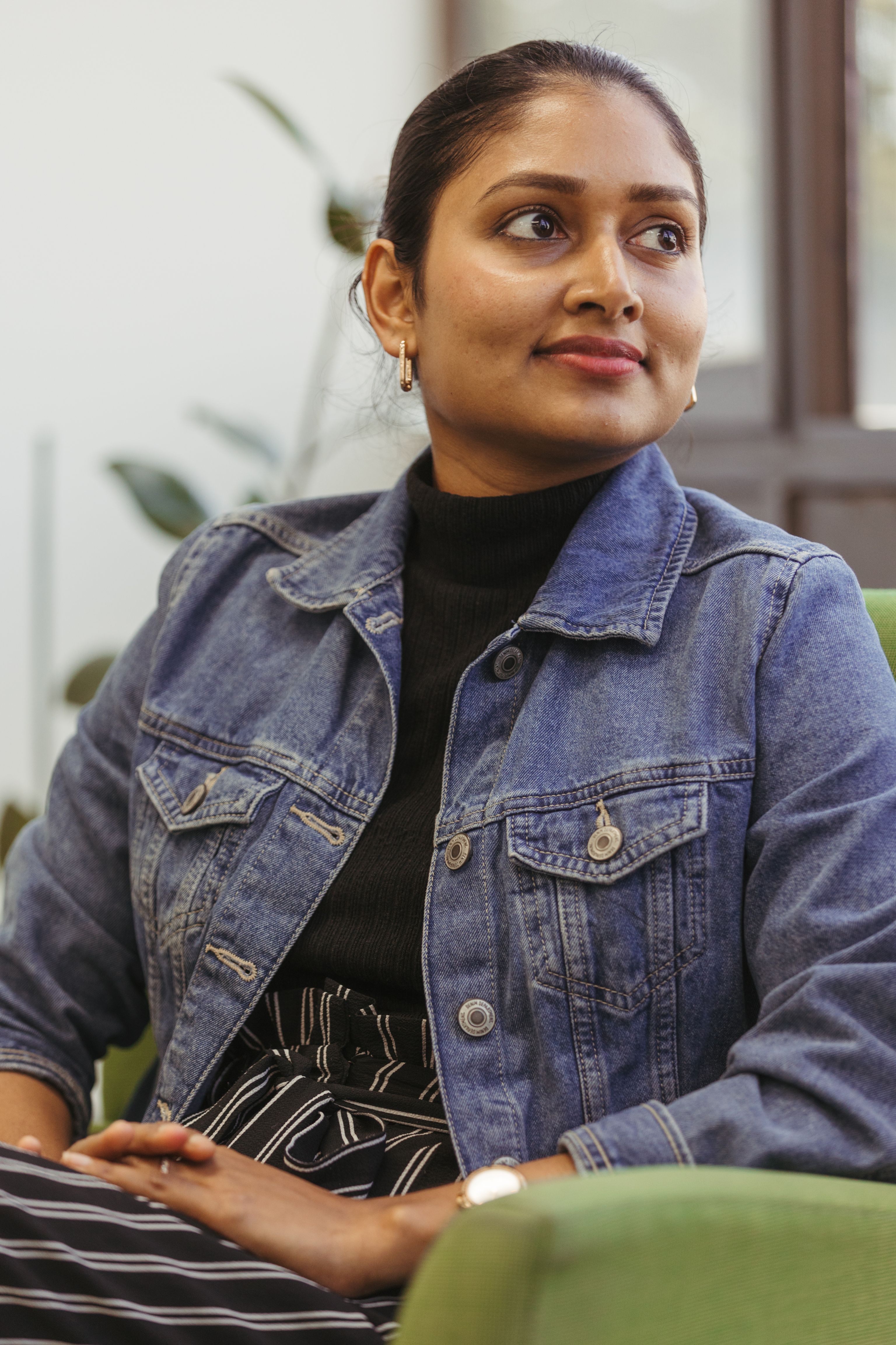 Young woman sitting on a chair indoors looking out of the window, with a pensive look on her face