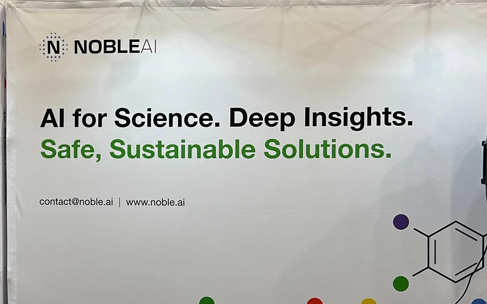 A NobleAI trade show backdrop reading 'AI for Science. Deep Insights. Safe, Sustainable Solutions.' under the company logo, with the molecule motif running across the bottom.