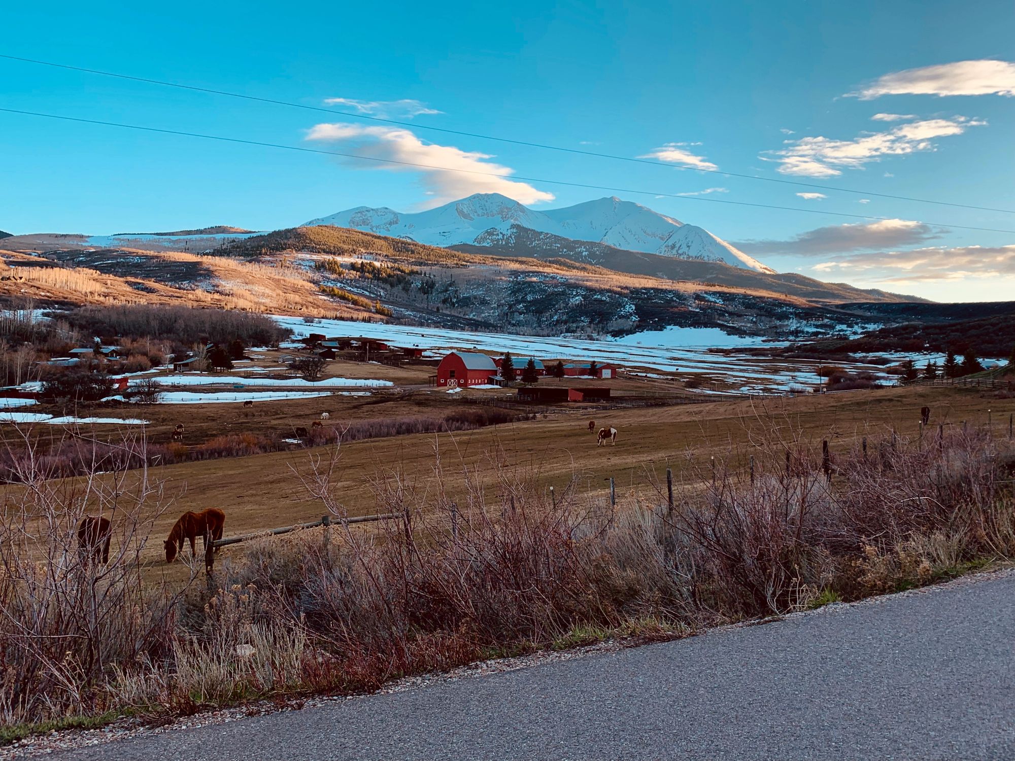 Horses beside a rustic barn beneath the mountains in Snowmass, Colorado.