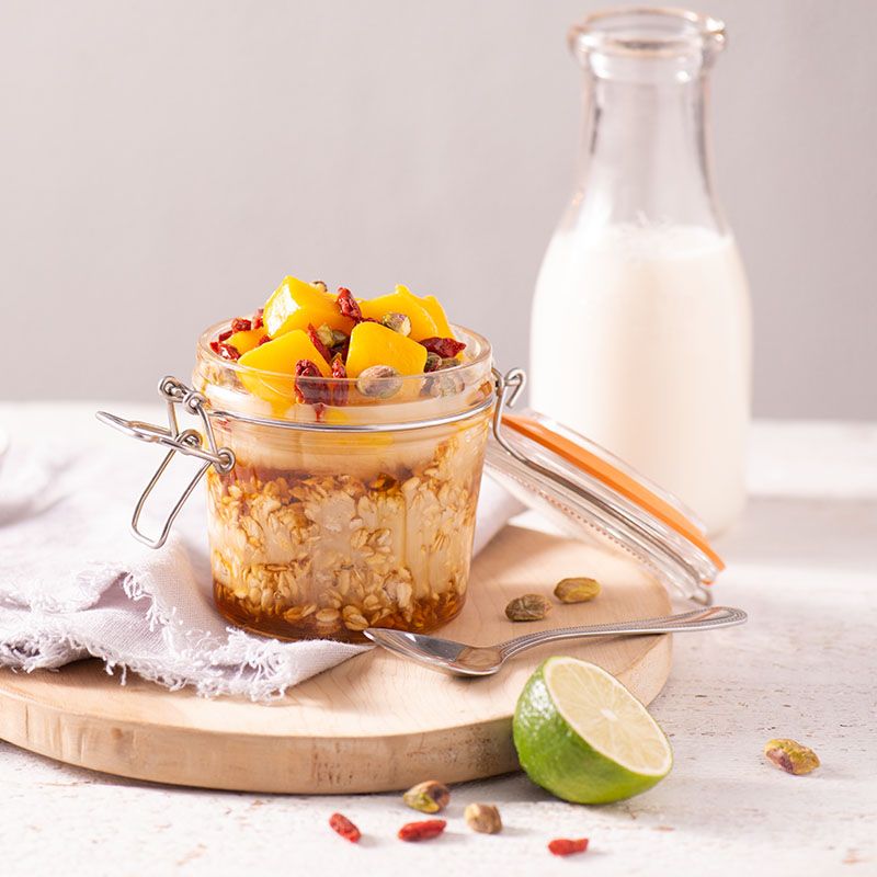 a jar of overnight oats with fruit and nuts on a wooden cutting board next to a bottle of milk .