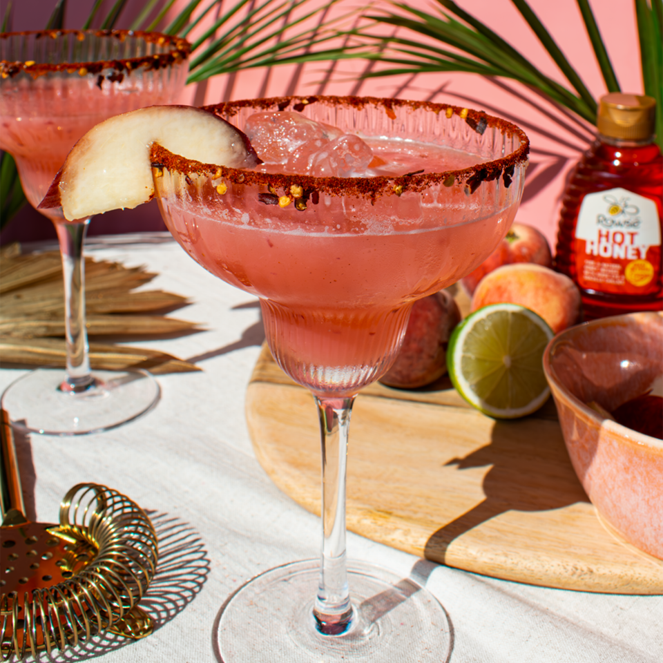 a bottle of hot honey sits next to a margarita