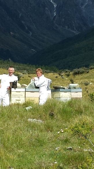 two men are standing in a field with beehives in the background .