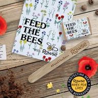 a wooden stick with the words `` feed the bees '' engraved on it is sitting on a wooden table next to a book .