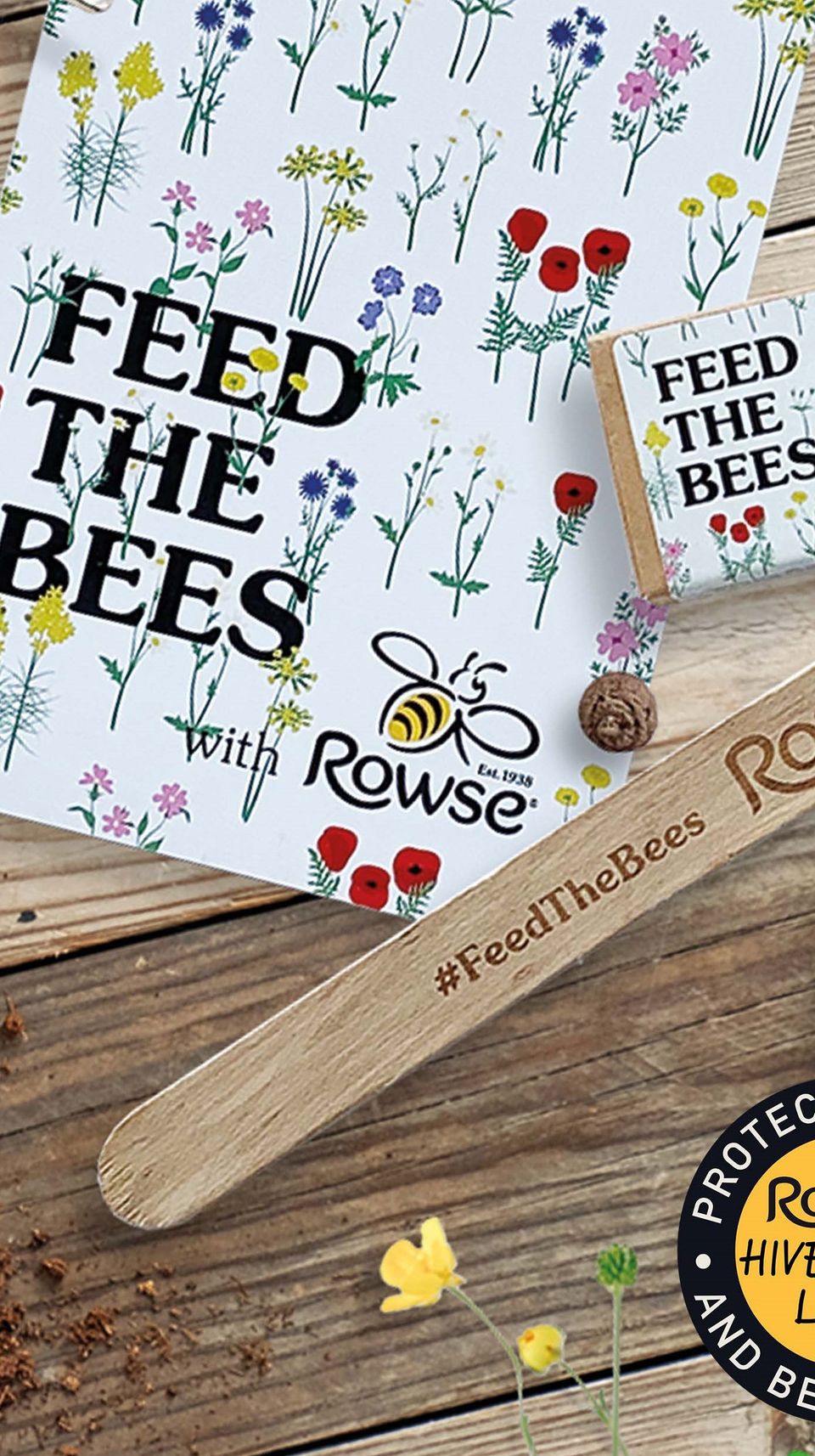 a wooden stick with the words `` feed the bees '' engraved on it is sitting on a wooden table next to a book .