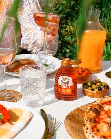 a bottle of hot honey sits on a table next to pizza