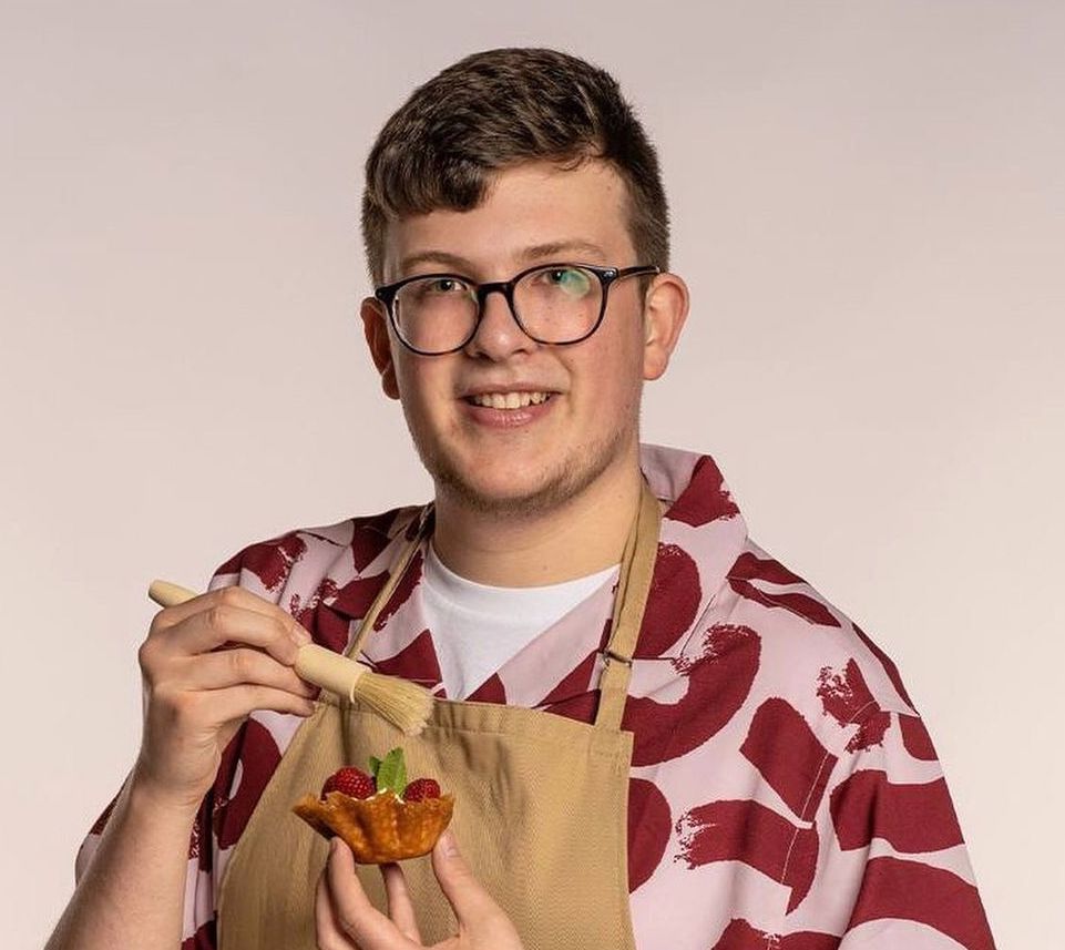 a young man in an apron is holding a piece of food and a brush .