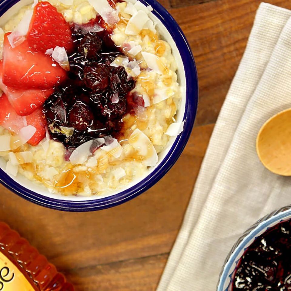 a bowl of oatmeal with strawberries and blueberries next to a bottle of honey .