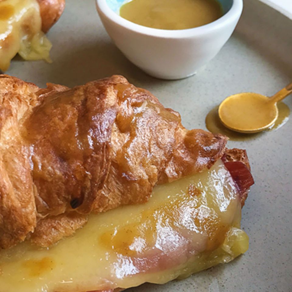 a close up of a croissant with cheese and ham on a plate with a spoon