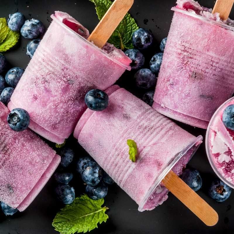 a close up of ice cream popsicles with blueberries and mint leaves on a table .