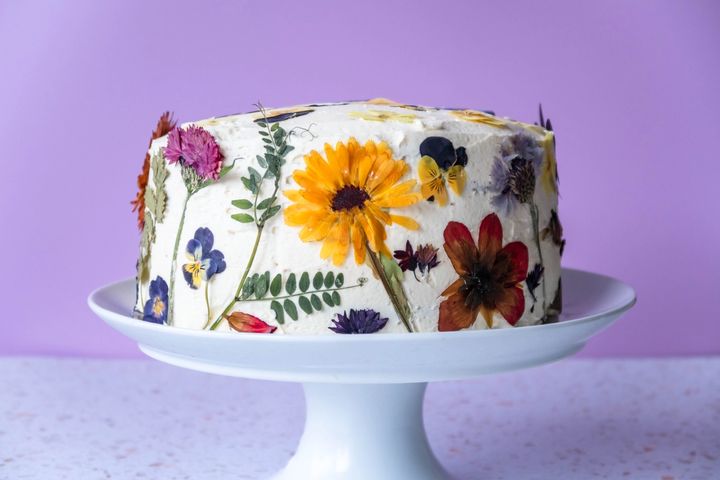 a cake decorated with dried flowers on a white plate on a cake stand .