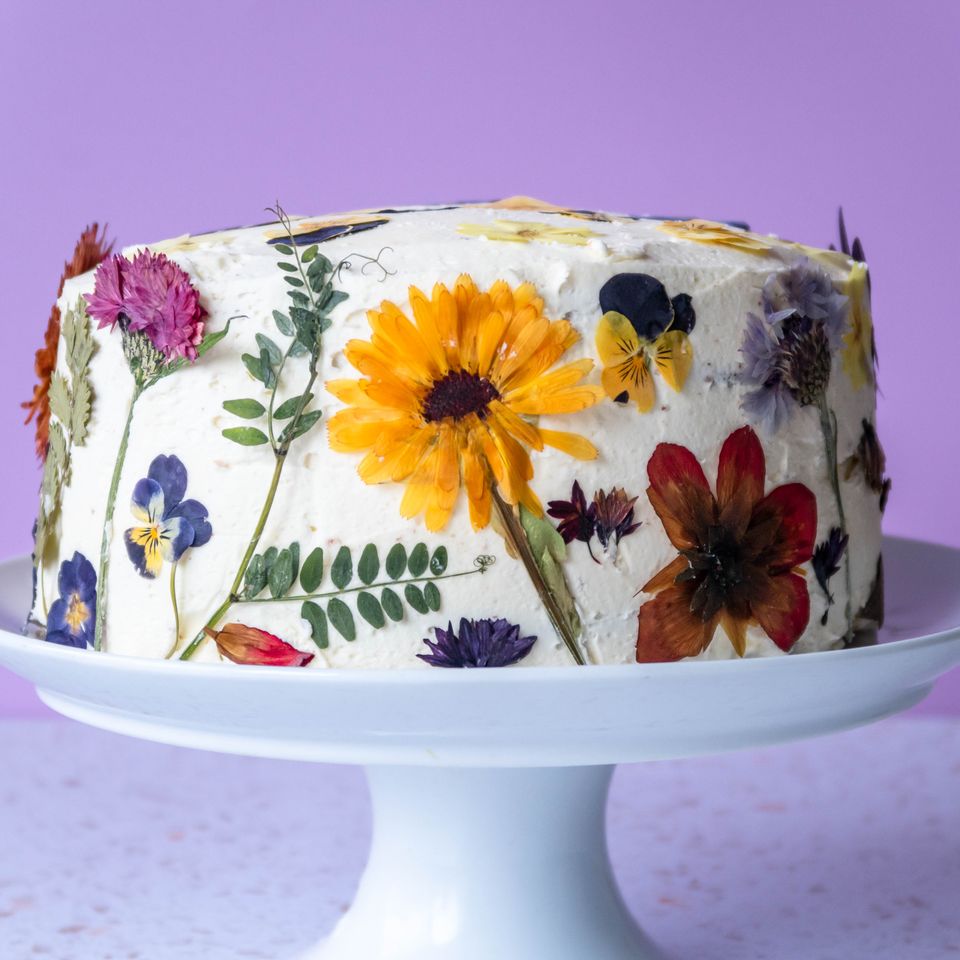 a cake decorated with dried flowers on a white plate on a cake stand .