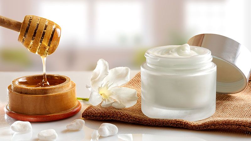 honey is being poured into a jar of cream on a table .