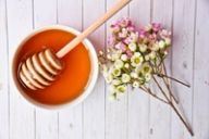 a bowl of honey with a honey dipper and flowers on a wooden table .