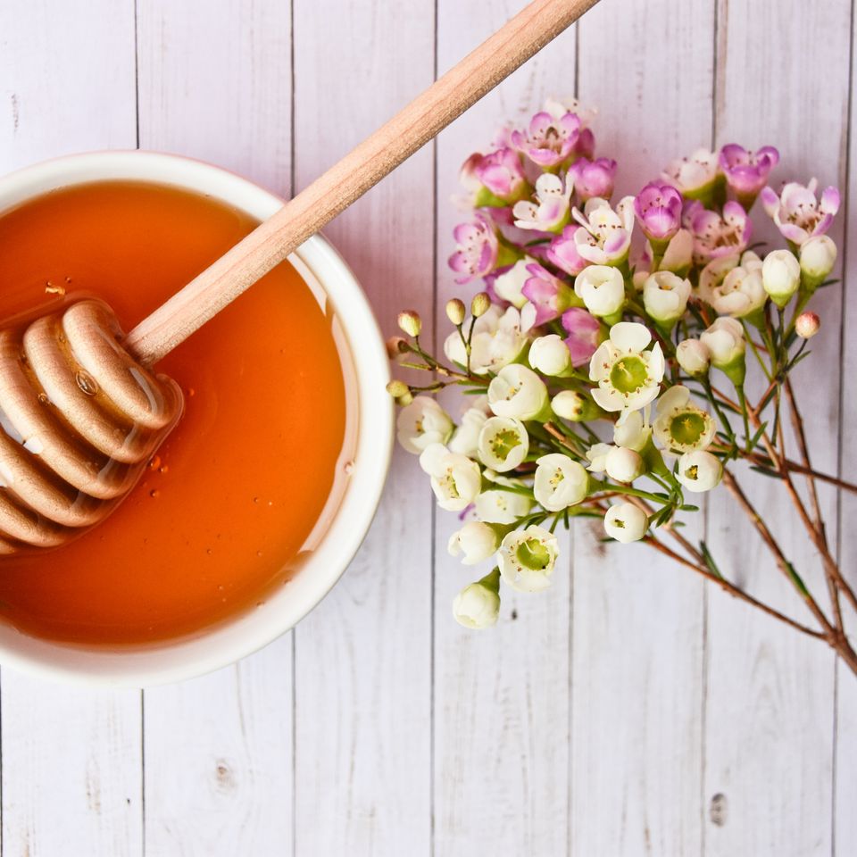a bowl of honey with a honey dipper and flowers on a wooden table .
