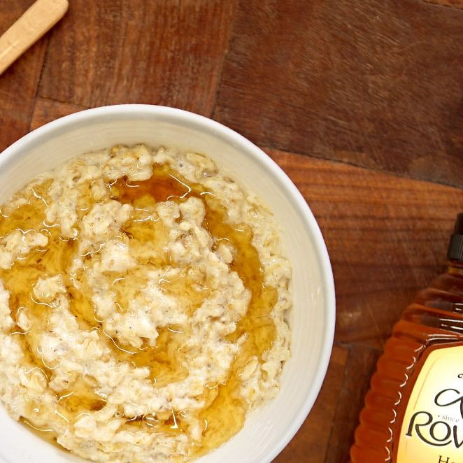 a bowl of oatmeal with honey and a Rowse bottle of honey on a wooden table .