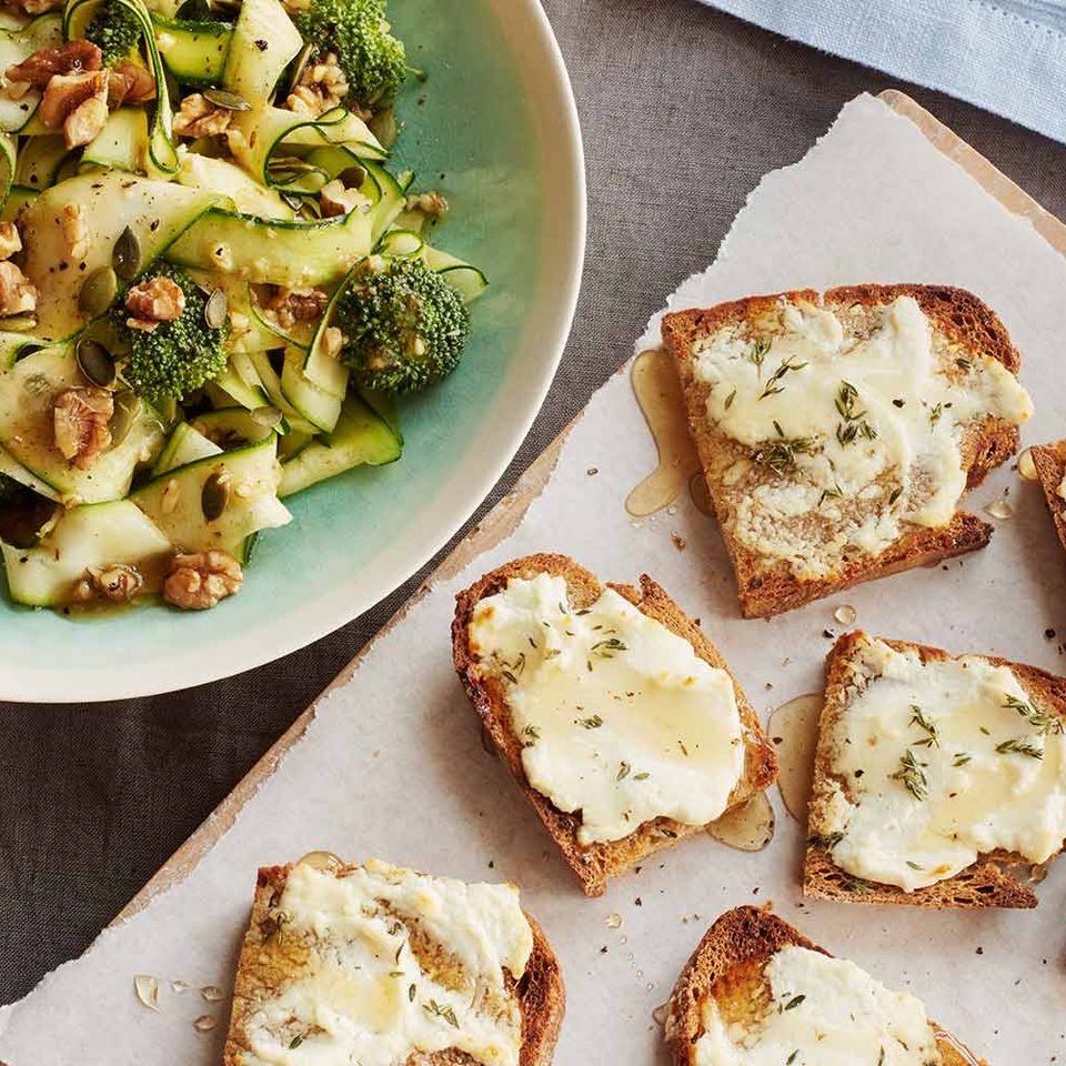 there is a bowl of broccoli and zucchini salad next to a plate of toast .
