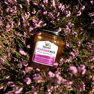 a jar of heather max honey is surrounded by purple flowers .
