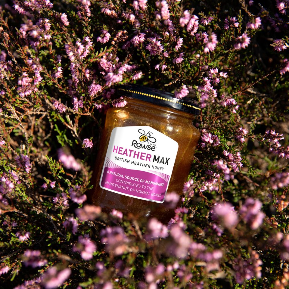 a jar of heather max honey is surrounded by purple flowers .