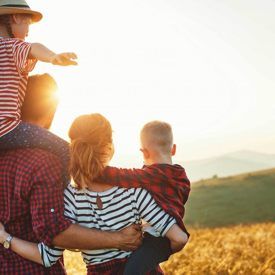 a man is carrying two children on his shoulders in a field .