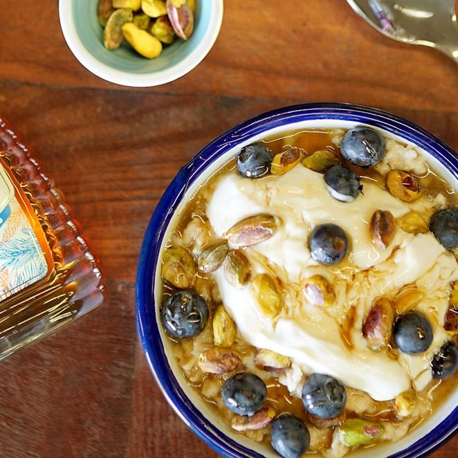 a bowl of oatmeal with yogurt , blueberries and pistachios next to a bottle of honey .
